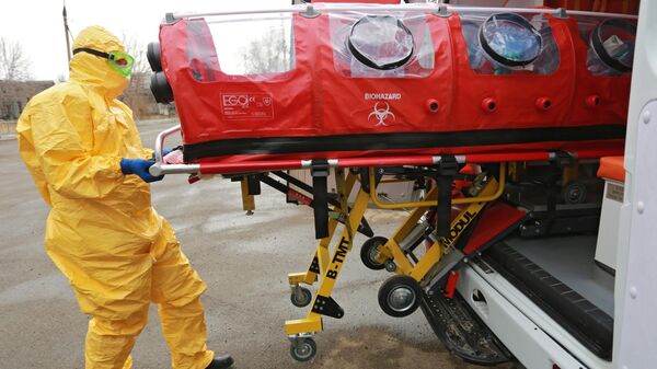  Врач бригады скорой помощи в защитном костюме загружает бокс для перевозки зараженных коронавирусом в машину