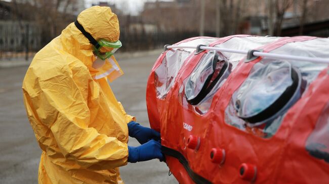 Врач бригады скорой помощи в защитном костюме готовит бокс для перевозки зараженных коронавирусом