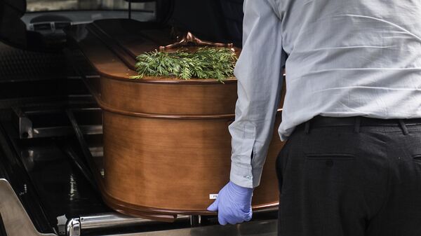 Грузчик достает гроб из катафалка на кладбище Альмудена в Мадриде