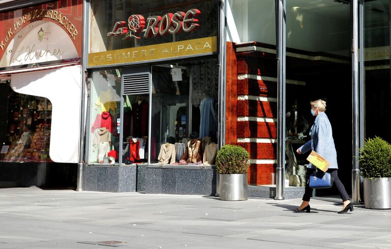 Женщина в защитной маске проходит мимо закрытых магазинов в Вене Женщина в защитной маске проходит мимо закрытых магазинов в Вене