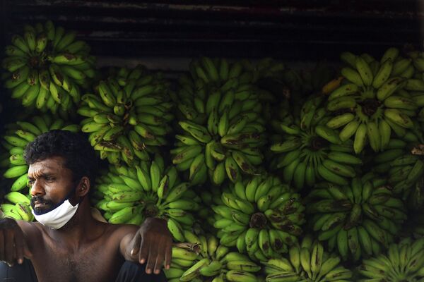 Рабочий в маске для лица отдыхает на овощном рынке в Коломбо