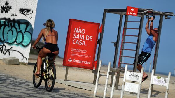 Девушка проезжает мимо баннера Не выходи из дома на пляже Ипанема в Рио-де-Жанейро во время пандемии коронавируса 