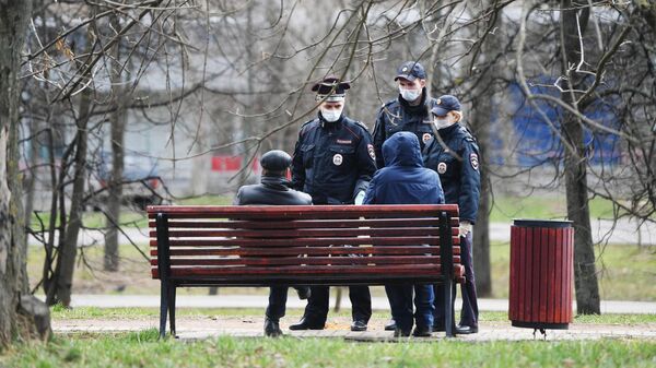 Сотрудники полиции разговаривают с людьми, сидящими на скамейке в сквере
