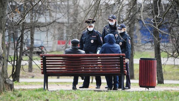 Сотрудники полиции разговаривают с людьми, сидящими на скамейке в сквере