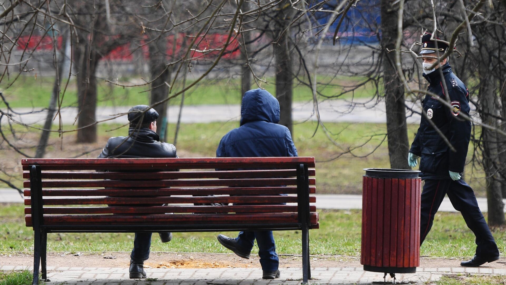 Сотрудник полиции подходит к людям, сидящим на скамейке в сквере - РИА Новости, 1920, 28.04.2021