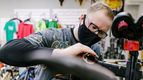 Мастер в защитной маске производит ремонт велосипеда в веломастерской