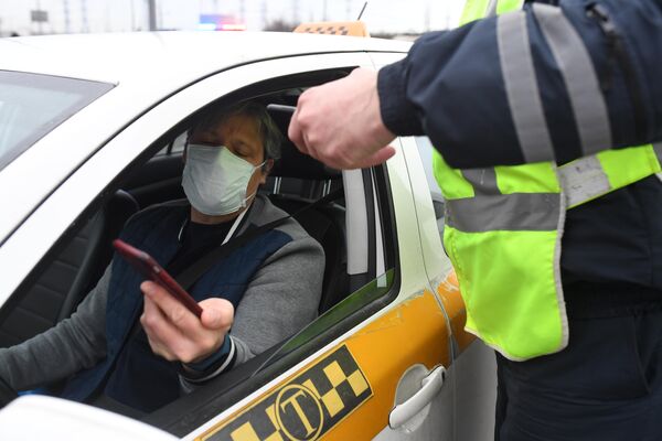 Сотрудник дорожно-патрульной службы ГИБДД во время проверки электронного пропуска у водителя такси на блокпосту при въезде в Москву