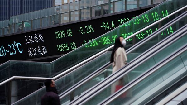 Люди в защитных масках проезжают на эскалаторе мимо табло с индексами Шанхайской и Шэньчжэньской фондовых бирж