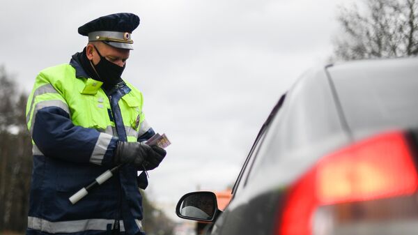 Инспектор дорожно-патрульной службы проверяет у водителя цифровой пропуск на передвижение