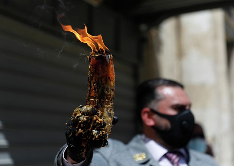 Мужчина в защитной маске держит свечу, зажженную от Благодатного огня в храме Гроба Господня в Иерусалиме