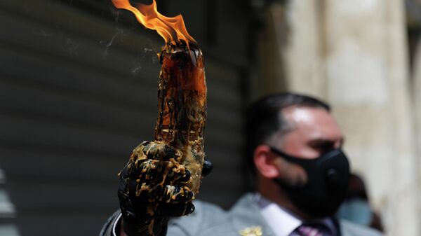 Мужчина в защитной маске держит свечу, зажженную от Благодатного огня в храме Гроба Господня в Иерусалиме
