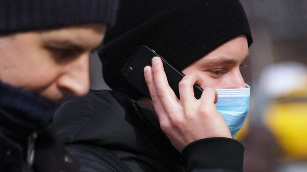 Молодой человек в медицинской маске разговаривает по телефону