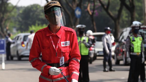 Член Индонезийского Красного Креста на полицейском КПП после введения ограничений в связи с распространением коронавируса