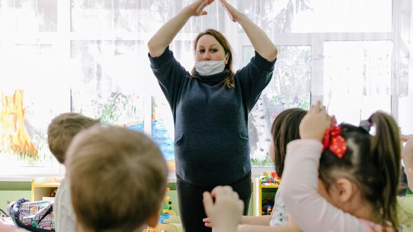 Воспитатель в медицинской маске играет с детьми в детском саду