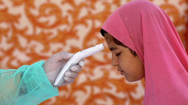 Медицинский работник измеряет температуру у девочки в центре тестирования на коронавирус в Карачи, Пакистан