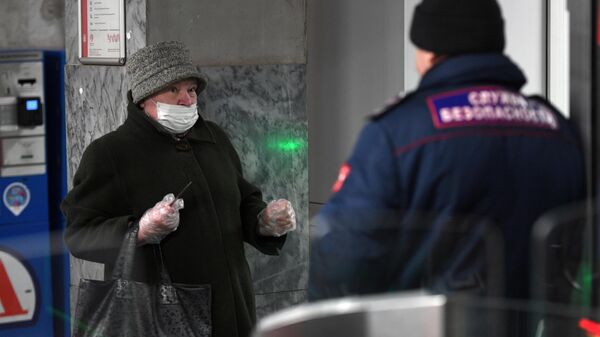 Женщина в защитной маске разговаривает с сотрудником службы безопасности на станции метро Тушинская в Москве