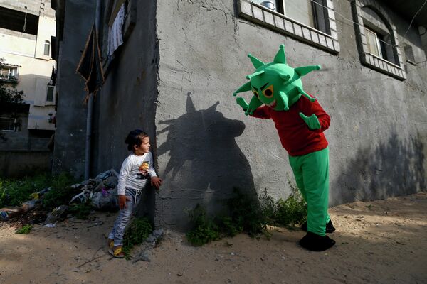 Палестинец, одетый в костюм коронавируса играет с девочкой в центральной части Сектора Газа