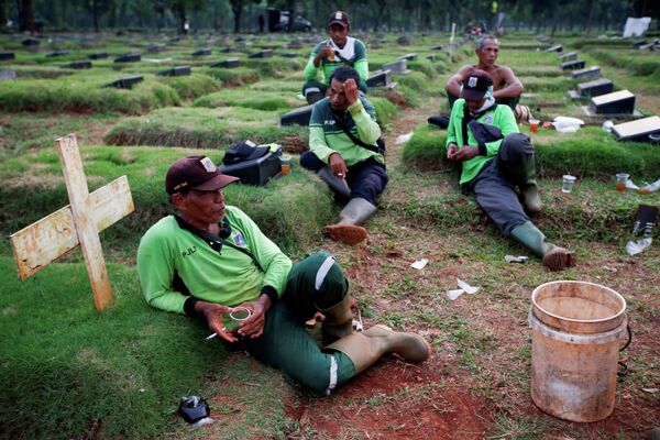 Могильщики отдыхают в перерыве между работой на кладбище в Джакарте, Индонезия 