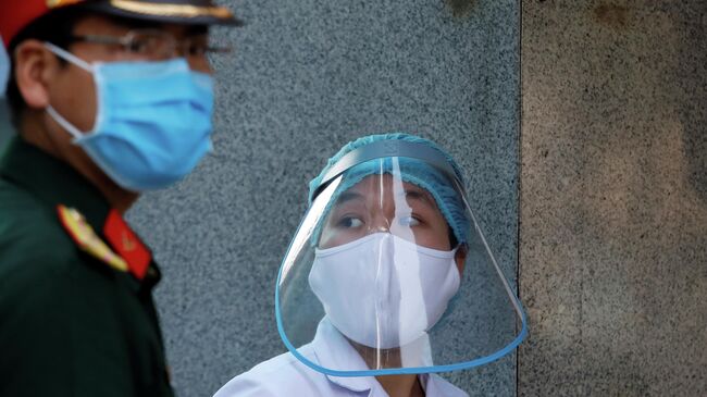 Медицинский работник в защитной маске рядом с солдатом, возле больницы во время вспышки коронавирусна в Ханое, Вьетнам