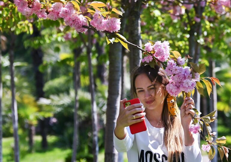 Девушка фотографируется на мобильный телефон на аллее Черешневый сад в Сочи