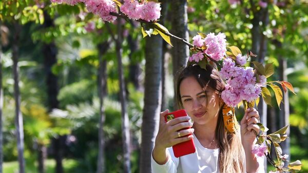 Девушка фотографируется на мобильный телефон на аллее Черешневый сад в Сочи