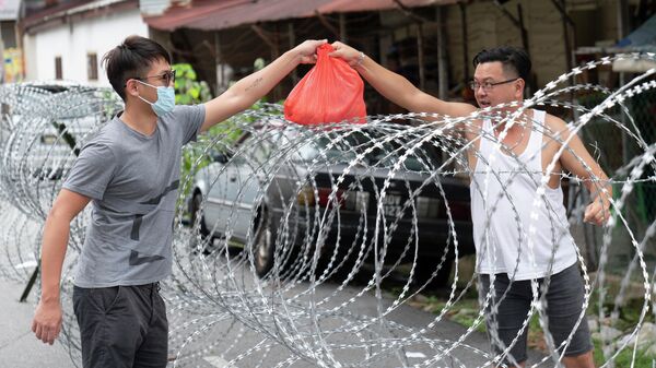 Мужчина передает пакет через колючую проволоку в закрытом районе Селаянг-Бару, недалеко от Куала-Лумпура, Малайзия