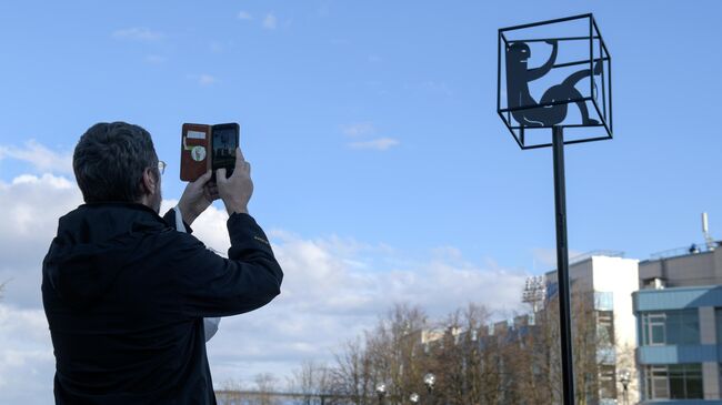 Мужчина фотографирует памятник самоизоляции в виде куба с силуэтами человека и кошки в Санкт-Петербурге
