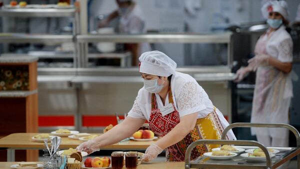 Работница школьной столовой разносит тарелки с едой