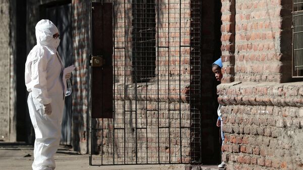 Женщина в защитном костюме разговаривает с ребенком в мигрантском районе во время введения карантинного режима в Сантьяго