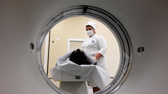 Медицинский работник готовит пациентку к проведению компьютерной томографии 