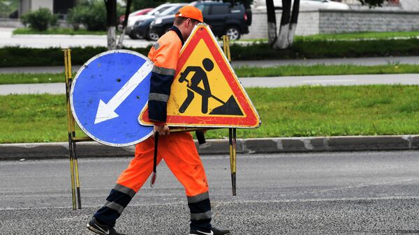 Рабочий переносит дорожные знаки во время укладки верхнего слоя дорожного покрытия