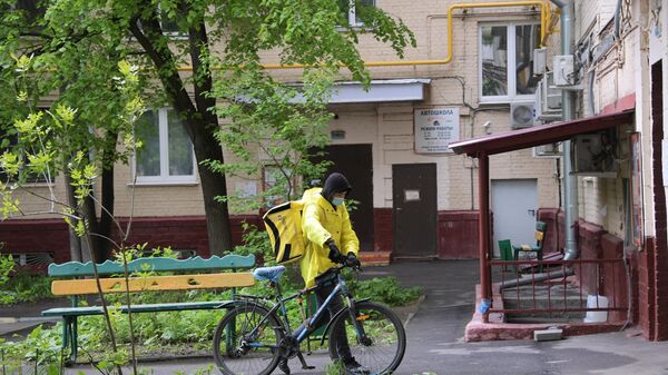 Курьер службы доставки Яндекс Еда у подъезда жилого дома на Ленинском проспекте в Москве