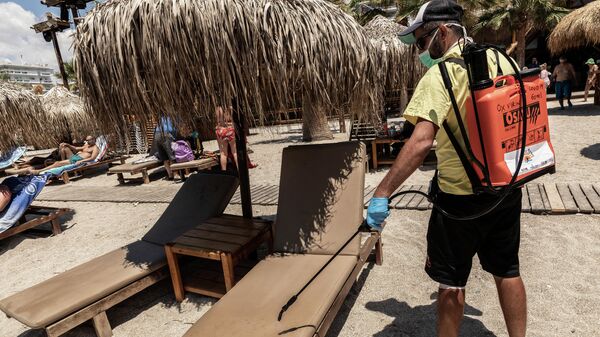 Рабочий дезинфицирует лежаки на городском пляже Алимос в пригороде Афин