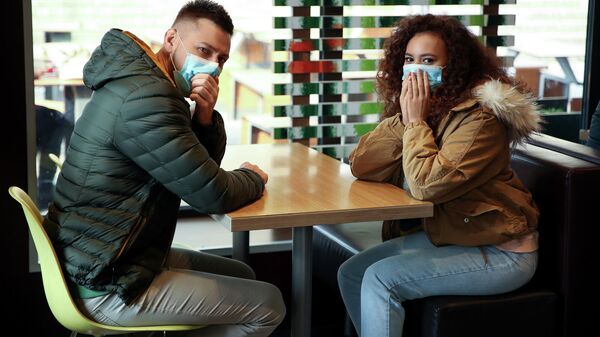 Молодые люди в защитных медицинских масках за столиком в кафе