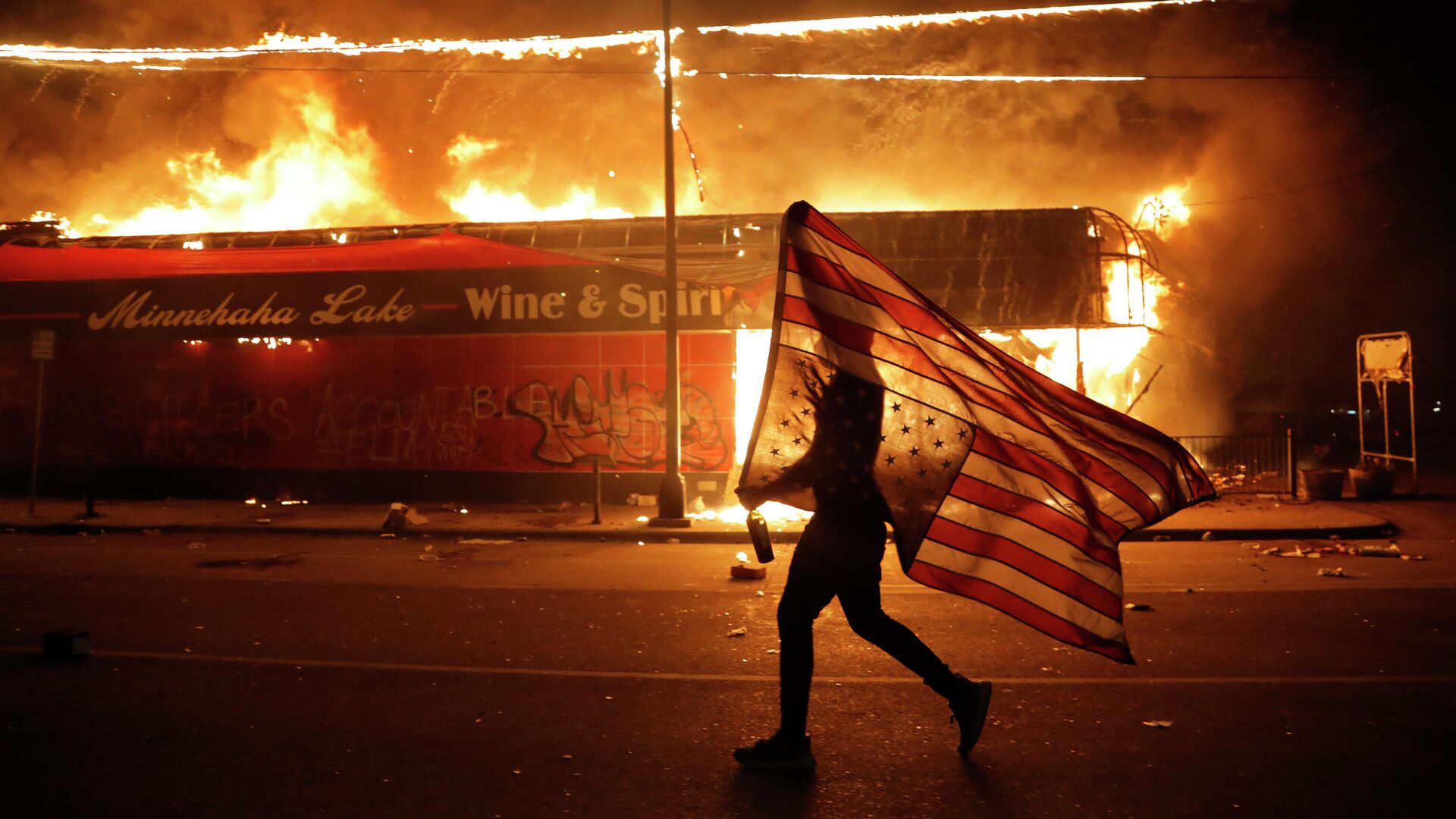 Протестующий несет перевернутый американский флаг возле горящего здания в Миннеаполисе - РИА Новости, 1920, 31.05.2020