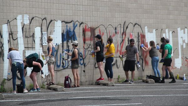 Люди закрашивают граффити на стене здания после беспорядков на Лейк-стрит в Миннеаполисе