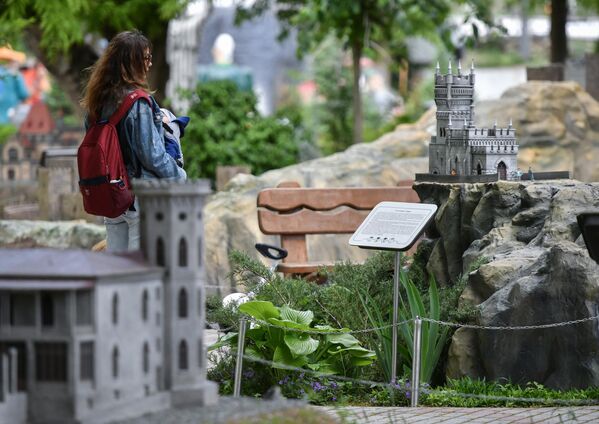 Женщина с ребенком у макета Памятника архитектуры Ласточкино гнездо в Бахчисарайском парке Крым в миниатюре на ладони