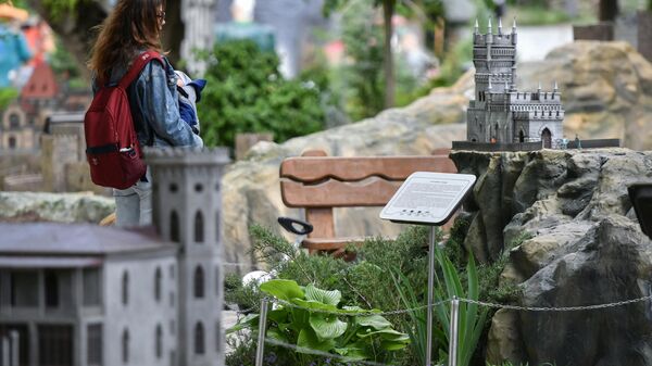 Женщина с ребенком у макета Памятника архитектуры Ласточкино гнездо в Бахчисарайском парке Крым в миниатюре на ладони