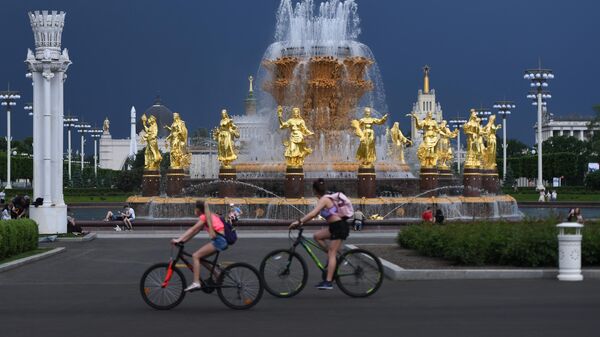 Посетители ВДНХ проезжают на велосипедах мимо фонтана Дружба народов