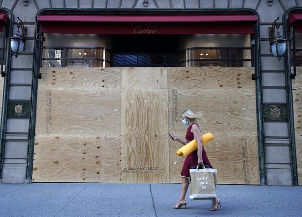 Девушка проходит мимо заколоченных витрин магазина Cartier на пятой авеню в Нью-Йорке