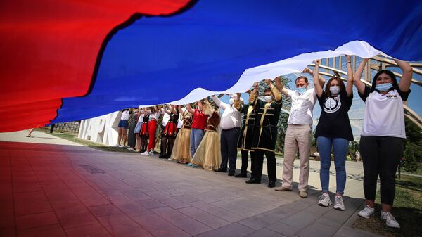 Участники празднований Дня России держат российский флаг в парке Дружбы города Георгиевска Ставропольского края