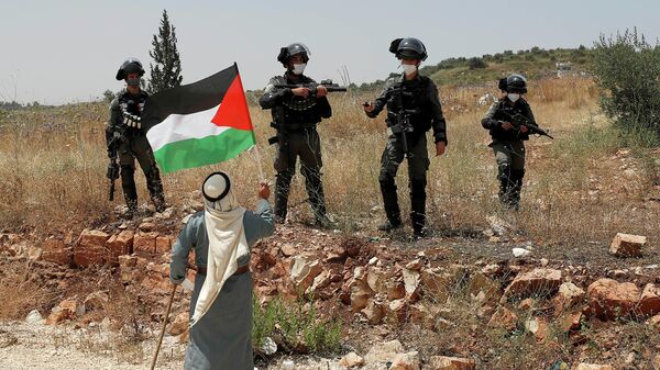 Протестующий против аннексии территорий Западного берега реки Иордан держит флаг Палестины перед израильскими военными