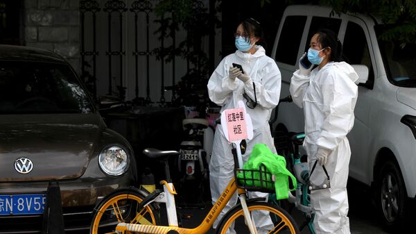 Девушки в защитных костюмах рядом с местом, где берут тест мазок на коронавирус у людей живущих рядом или посещающих рынок Синьфади