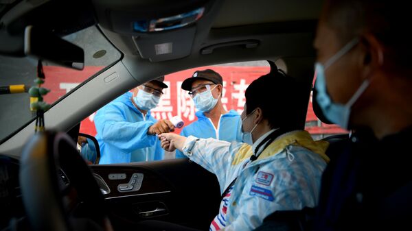 Сотрудник Службы безопасности в защитном костюме проверяет температуру людей, въезжающих на рынок Синьфади в Пекине, Китай