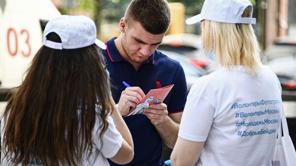 Молодой человек пишет пожелания на открытке возле в арт-объекта, установленного в рамках акции Добрые бейджи на Тверской улице в Москве
