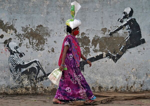 Женщина в защитной маске проходит мимо граффити после ослабления карантинных мер в Мумбаи
