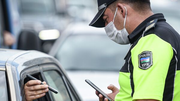 Полицейский проверяет документы у водителя автомобиля в Баку