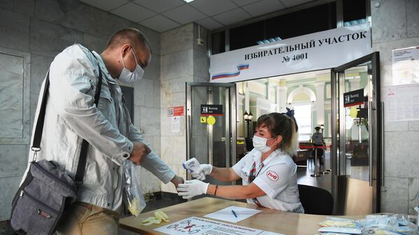 Мужчине измеряют температуру, перед тем как он проголосует по одобрению внесения поправок в Конституцию РФ на избирательном участке на Курском вокзале в Москве