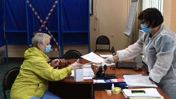 Женщина получает бюллетень на избирательном участке во время голосования по внесению поправок в Конституцию РФ