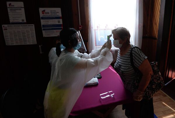 Женщине измеряют температуру при входе на избирательный участок №81 в сельском клубе поселка Усть-Мана Красноярского края, где проводится голосование по внесению поправок в Конституцию РФ 